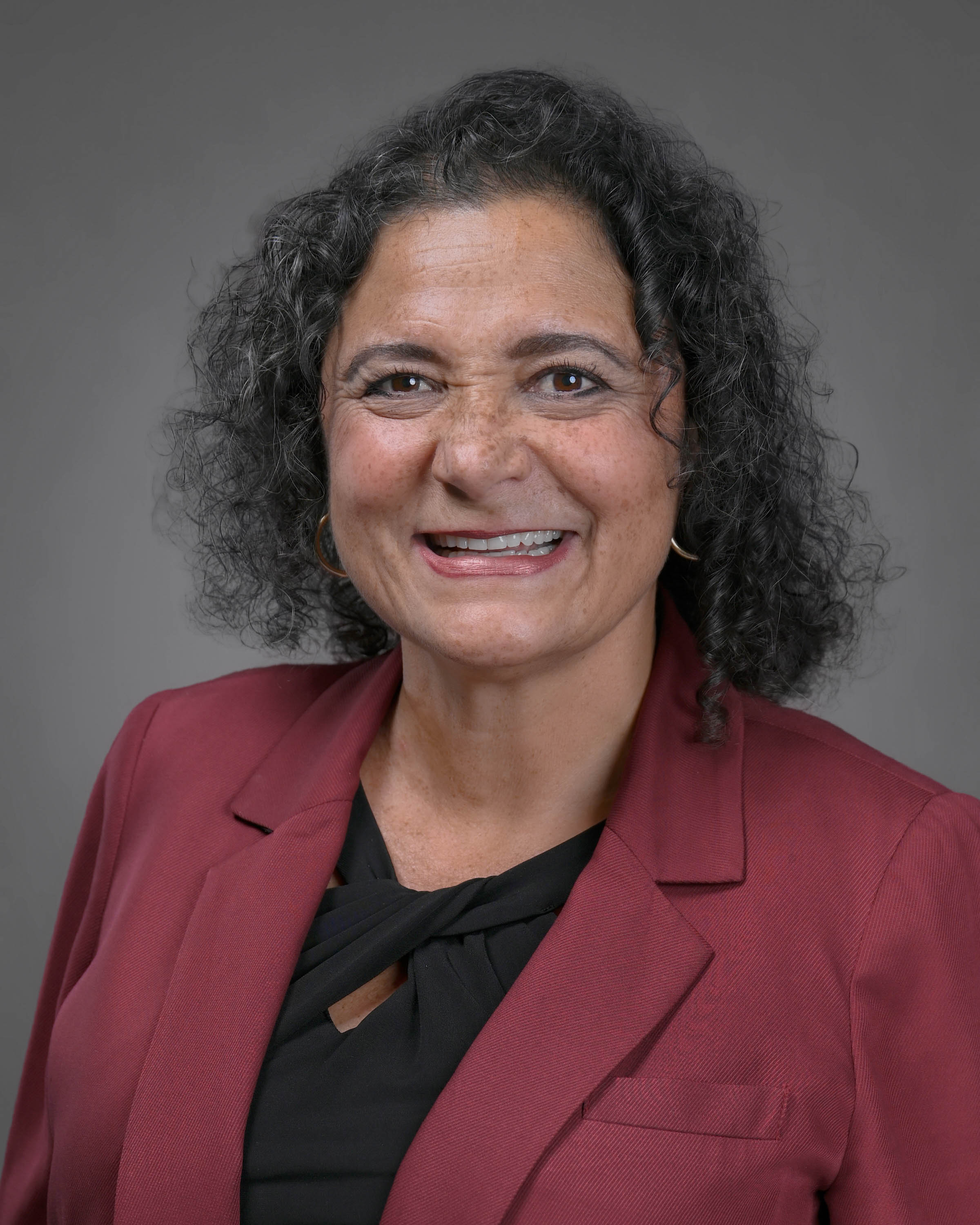 Smliing woman with dark curly brown hair and a red jacket with black shirt